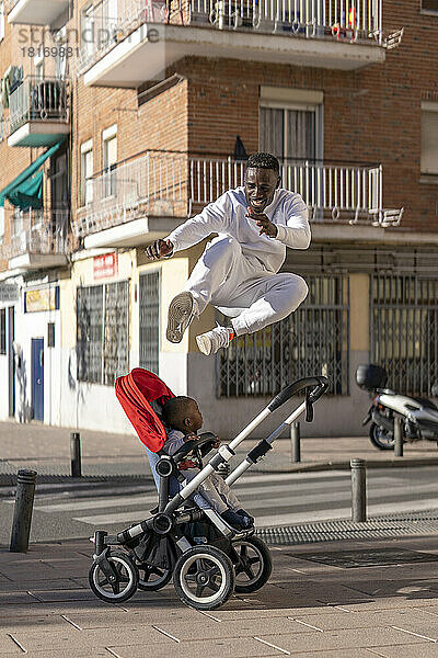 Junger Mann springt vor Baby im Kinderwagen auf Fußweg