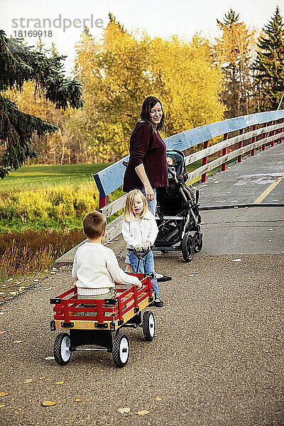Eine Mutter und ihre kleinen Kinder überqueren eine Brücke über einen Fluss in einem Stadtpark während der Herbstsaison; ihre kleine Tochter hat das Down-Syndrom; St  Albert  Alberta  Kanada