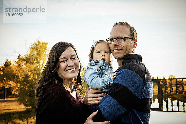 Familienporträt auf einer Brücke über einen Fluss in einem Stadtpark während der Herbstsaison; ihre kleine Tochter hat das Down-Syndrom; St. Albert  Alberta  Kanada