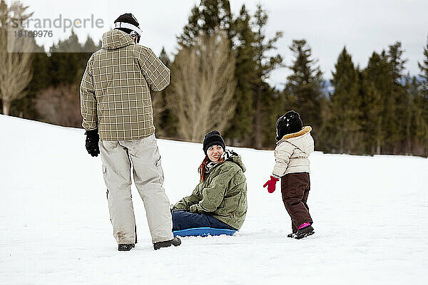 Vater  Mutter und junge Tochter mit Schlitten auf einem verschneiten Hügel in einem Bergferienort; Fairmont Hot Springs  British Columbia  Kanada