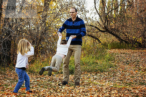 Ein Vater schaukelt seinen Sohn herum und verbringt viel Zeit mit seinen Kindern bei einem Familienausflug in einem Stadtpark im Herbst; St. Albert  Alberta  Kanada