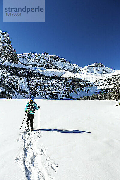 Frau beim Schneeschuhwandern auf einem unberührten schneebedeckten See mit schneebedeckten Rocky Mountains im Banff National Park; Lake Louise  Alberta  Kanada