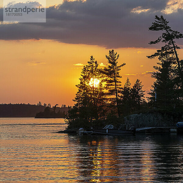 Goldener Sonnenuntergang über einem schönen See mit Motorboot und Dock entlang der Uferlinie  Lake of the Woods  Ontario; Ontario  Kanada