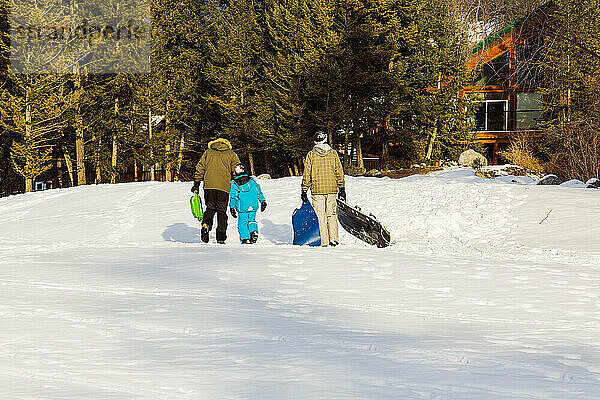 Zwei Männer gehen mit einem Kind spazieren  nachdem sie in einem Bergdorf gerodelt sind; Fairmont Hot Springs  British Columbia  Kanada