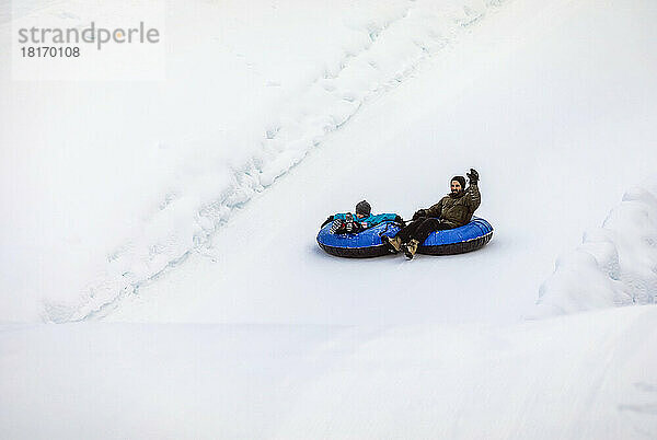 Vater und Sohn beim Tubing auf einem Skihügel; Fairmont Hot Springs  British Columbia  Kanada