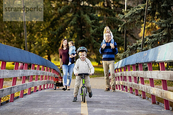 Junge Familie überquert eine Brücke über einen Fluss in einem Stadtpark während der Herbstsaison; ihre kleine Tochter hat das Down-Syndrom; St. Albert  Alberta  Kanada