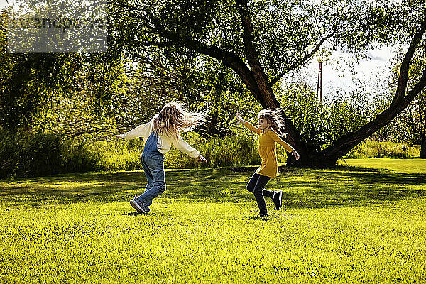 Zwei Schwestern genießen die Gesellschaft des anderen und spielen und drehen sich an einem warmen Herbsttag in einem Stadtpark; St. Albert  Alberta  Kanada
