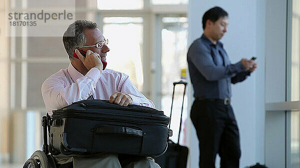 Mann mit Rückenmarksverletzung in einem Rollstuhl auf einem Flughafen  während ein Passagier vorbeifährt; Massachusetts  Vereinigte Staaten von Amerika