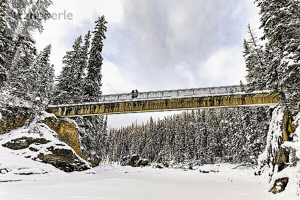 Zwei ältere Frauen  die im Winter den Fußgängerweg über den Kicking Horse River in der Nähe der Natural Bridge im Yoho National Park benutzen; British Columbia  Kanada