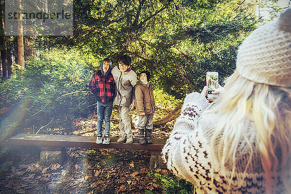 Eine Mutter fotografiert ihre drei Söhne auf einer Parkbank mit ihrem Smartphone  während sie dumme Grimassen schneiden; Langley  British Columbia Kanada