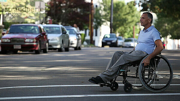 Mann mit Querschnittslähmung im Rollstuhl beim Überqueren der Straße an einem barrierefreien Zugang; Massachusetts  Vereinigte Staaten von Amerika