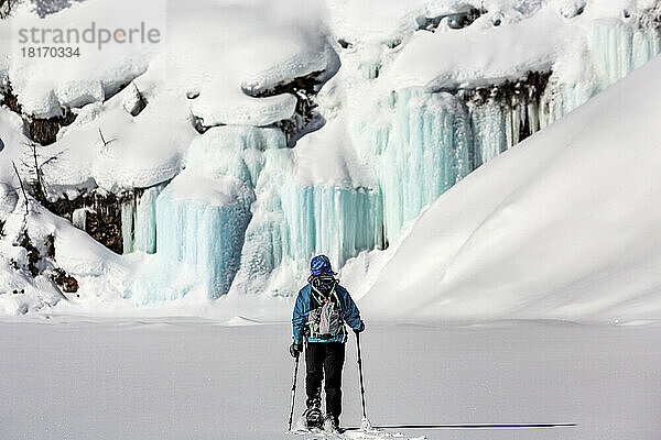 Frau beim Schneeschuhwandern auf einem unberührten  schneebedeckten See mit Eisfällen und schneebedeckten Felsen im Banff National Park; Lake Louise  Alberta  Kanada