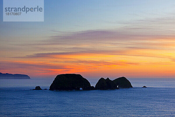 Winterlicher Sonnenuntergang und silhouettierte Felsformationen mit natürlichen Bögen  gesehen von Cape Meares an der Küste von Oregon  USA; Oregon  Vereinigte Staaten von Amerika
