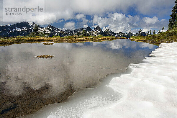 Alpiner Teich  in dem sich der Himmel spiegelt und der von Schnee gesäumt ist  mit den Tatoosh Mountains im Hintergrund  Mount Rainier National Park; Washington  Vereinigte Staaten von Amerika