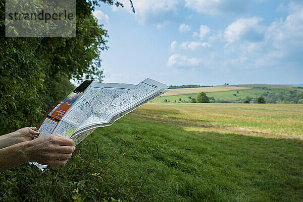 Hände halten eine Karte am Rande eines Feldes mit Blick auf die weite englische Landschaft; Rockbourne  Wiltshire  England