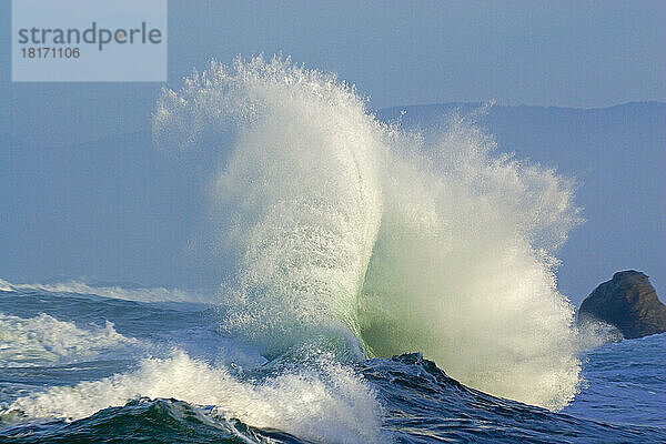 Dramatische  hoch aufspritzende Welle  die sich an der Küste bricht  mit der Küstenlinie von Oregon im Hintergrund am Cape Kiwanda; Pacific City  Oregon  Vereinigte Staaten von Amerika