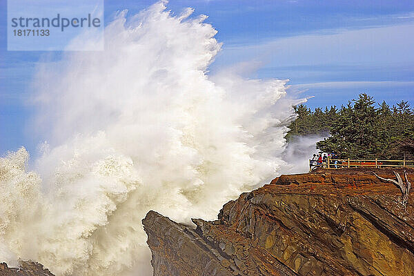 Mächtige Welle  die sich an den Felsen im Shore Acres State Park bricht  während Touristen an einem Aussichtspunkt stehen und das heftige Platschen beobachten  Küste von Oregon; Oregon  Vereinigte Staaten von Amerika