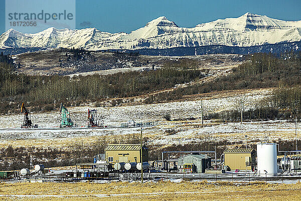Kompressorstation mit Pumpstationen im Hintergrund  schneebedeckter Hang und Bergkette mit blauem Himmel  nördlich von Longview  Alberta; Alberta  Kanada