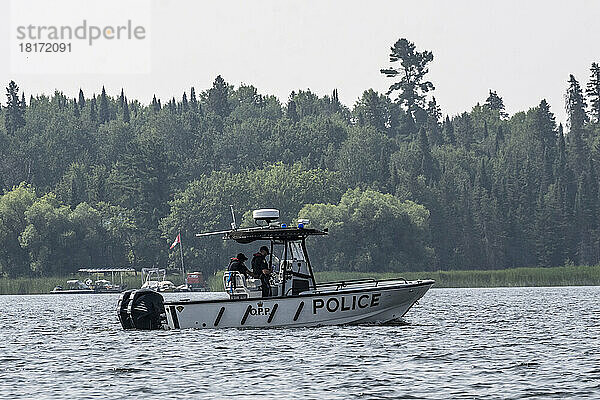 Polizeiboot  das am Ufer eines Sees entlang fährt  vorbei an Booten und Docks  Lake of the Woods; Kenora  Ontario  Kanada