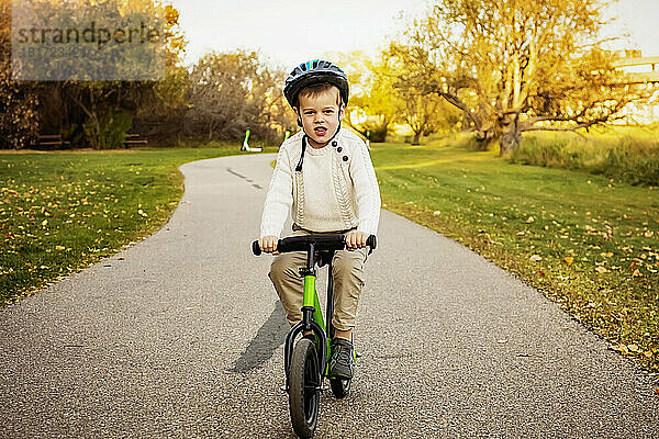 Young boy riding his bike on a path in a city park during a family outing in the fall season; St. Albert  Alberta  Canada