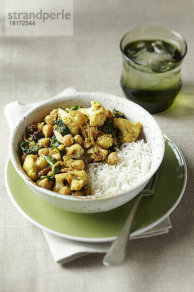 Schüssel mit Blumenkohl-  Kichererbsen- und Spinat-Curry mit weißem Reis und einem Glas Wasser