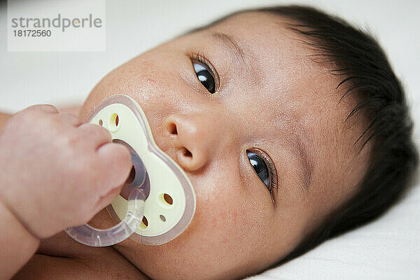 Nahaufnahme eines neugeborenen asiatischen Babys mit Babyakne mit Schnuller  Studioaufnahme auf weißem Hintergrund