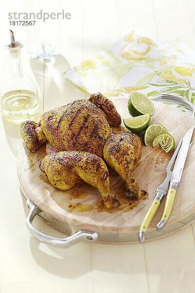 Gegrilltes Spatchcock-Hähnchen mit Gewürzeinreibung auf einem Holzbrett und Limettenspalten