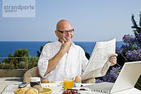 Mann auf der Terrasse frühstückt und liest Zeitung