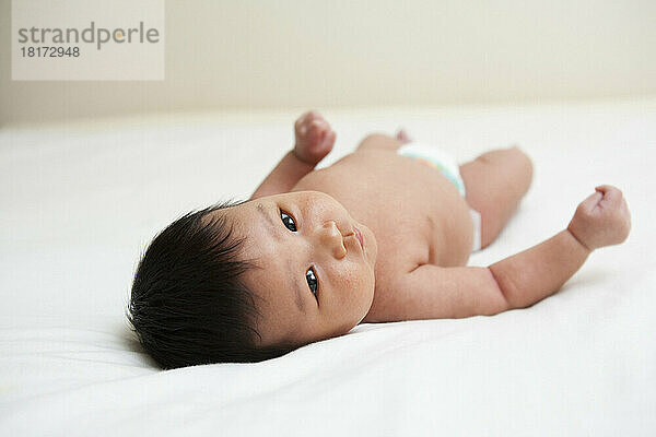 Newborn Asian baby in diaper  looking up at camera  studio shot on white background