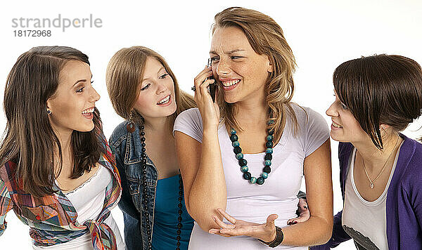 Vier junge Frauen lachen und schauen einander an  eine junge Frau benutzt ihr Mobiltelefon  Studioaufnahme auf weißem Hintergrund