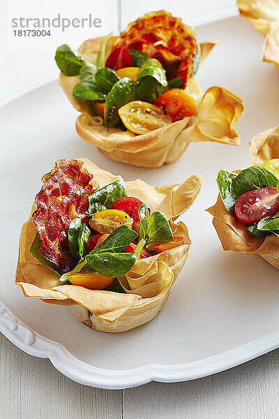 Speck- und Tomaten-Phyllo-Becher auf einer weißen Platte