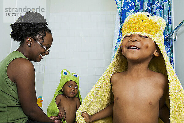 Mutter hilft Jungen beim Anziehen von Kapuzenhandtüchern nach dem Bad