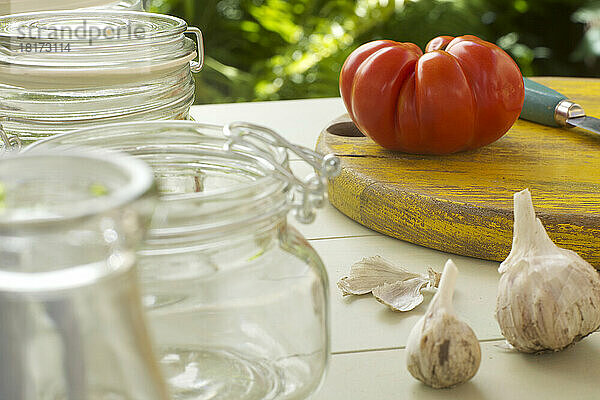Tomato on Cutting Board with Garlic and Glass Jars