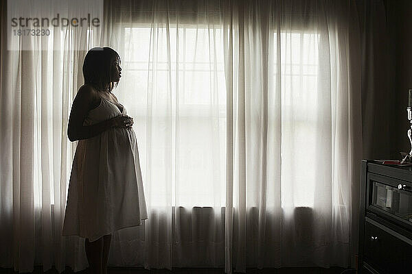 Silhouette einer schwangeren Frau  die aus dem Fenster schaut