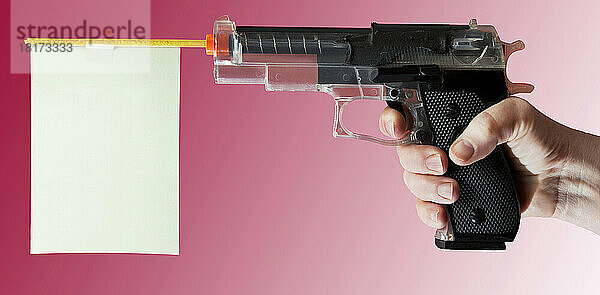 Nahaufnahme der Hand einer Frau  die auf eine Spielzeugpistole auf rosa Hintergrund zeigt  Studioaufnahme