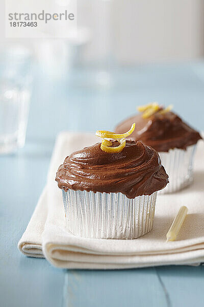 Cupcakes mit Schokoladenglasur  Zitronenschale und einer Kerze auf blauem Hintergrund