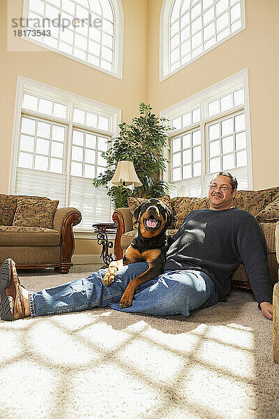 Porträt eines reifen Mannes mit seinem Haustier Rottweiler im Wohnzimmer