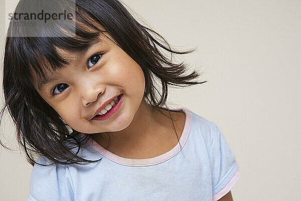 Nahaufnahmeporträt eines asiatischen Kleinkindmädchens  das in die Kamera blickt und lächelt  Studioaufnahme auf weißem Hintergrund
