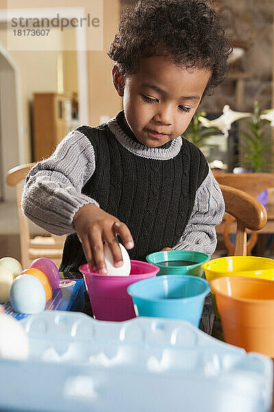 Junge benutzt Färbebecher  um Ostereier in der Küche zu färben