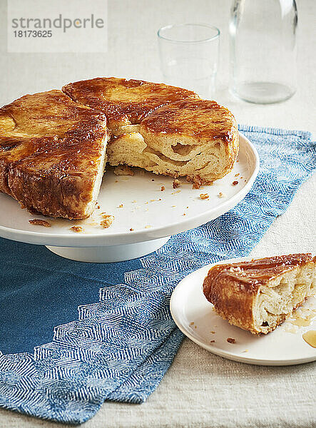 Kouign Amann auf einem Kuchenständer  ein Stück herausgenommen und auf einem Dessertteller davor serviert