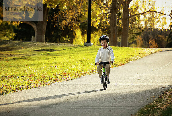 Kleiner Junge fährt während eines Familienausflugs im Herbst mit dem Fahrrad auf einem Weg in einem Stadtpark; St. Albert  Alberta  Kanada