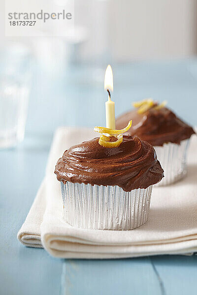 Cupcakes mit Schokoladenglasur  Zitronenschale und einer brennenden Geburtstagskerze auf blauem Hintergrund