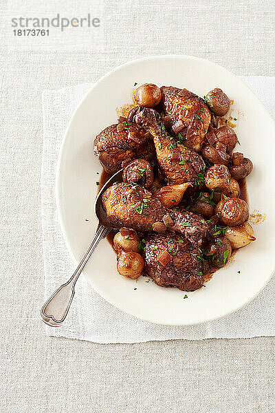 Hähnchen mit Weinsauce (Coq Au Vin) auf einer weißen Platte mit Servierlöffel