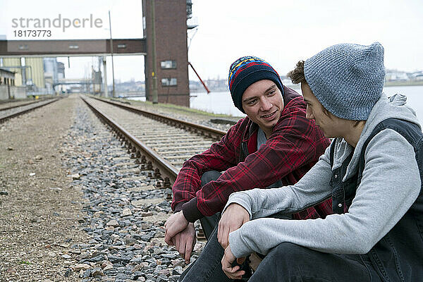 Zwei Teenager sitzen zusammen auf Eisenbahnschienen  in der Nähe des Hafens  Deutschland