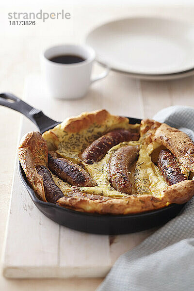 Frühstück mit Bratwurst und Pfannkuchen in einer gusseisernen Pfanne mit einer Tasse Kaffee