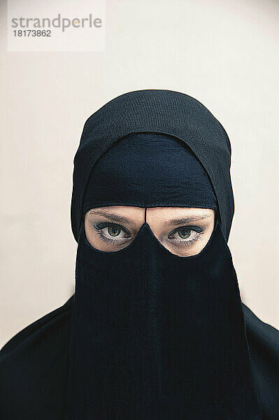 Nahaufnahme einer jungen Frau in schwarzem  muslimischem Hijab und muslimischer Kleidung  deren Augen in die Kamera blicken und Augen-Make-up zeigen  Studioaufnahme auf weißem Hintergrund