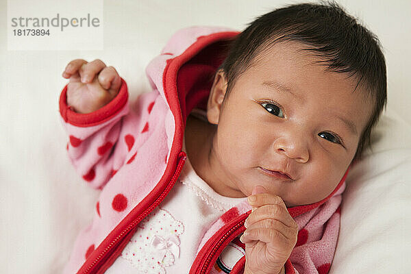 Close-up portrait of two week old Asian baby girl in pink polka dot jacket  smiling and looking at camera  studio shot