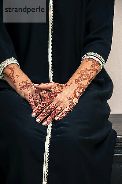 Frau sitzt drinnen mit Nahaufnahme von Armen und Händen  die im arabischen Stil mit Henna bemalt sind  trägt ein typisch schwarzes  arabisches  muslimisches Kleid  Studioaufnahme