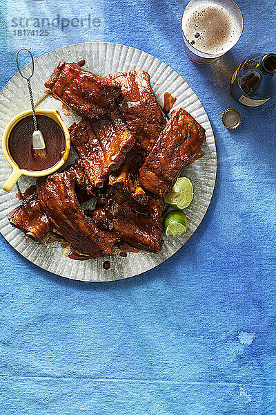 Langsam gegarte Rippchen mit Barbecue-Sauce und Bierflaschen auf blauem Hintergrund