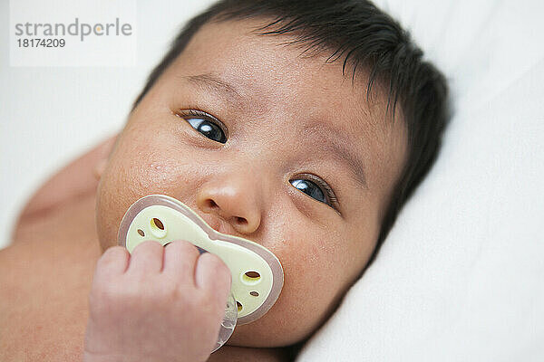 Nahaufnahme eines neugeborenen asiatischen Babys mit Babyakne mit Schnuller  Studioaufnahme auf weißem Hintergrund